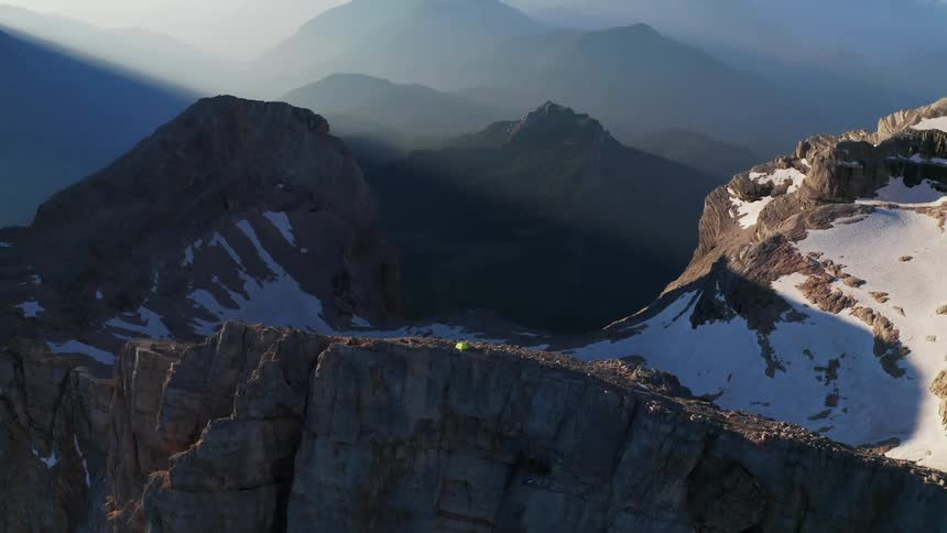 A bright neon yellow structure sits near the edge of a mountain side