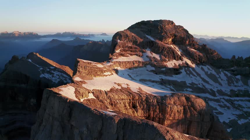 A mountain range with snow and mist in the horizon with shadows from the sun