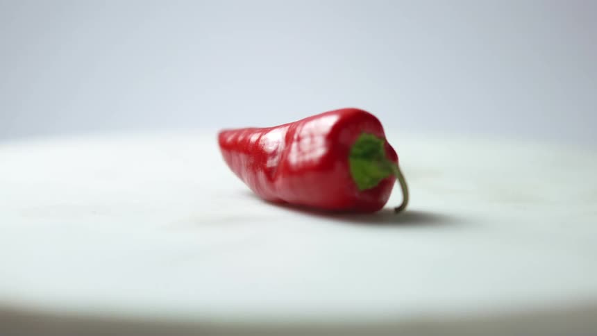 A camera spins around a red pepper in front of a white background