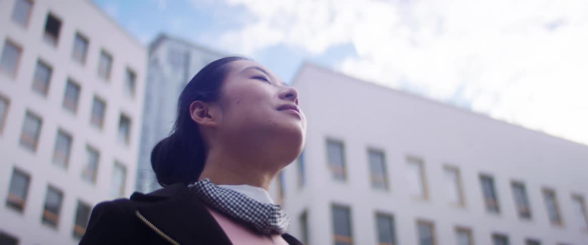 Asian woman with a blazer jacket and a scarf stands in front of buildings