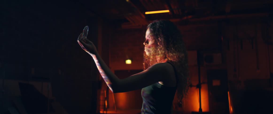 A woman holds a lens and extends it out from her body