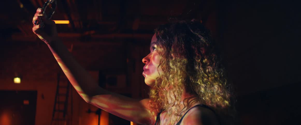 A woman stands on stage inside of a theater and raises a shiny object above her and stares curiously