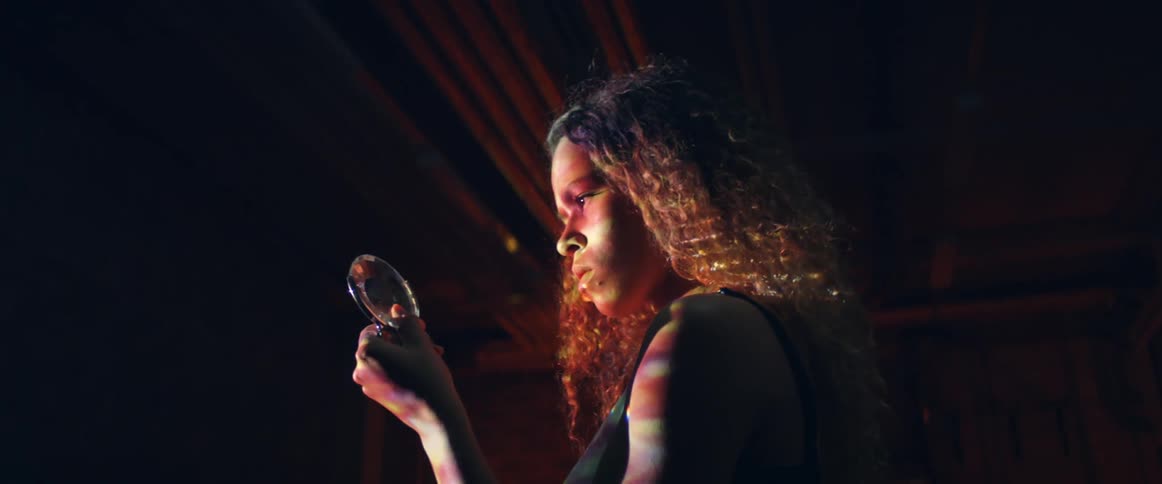 Woman stands in dark room turning a piece of glass to make the refection move with colored lights on her arm
