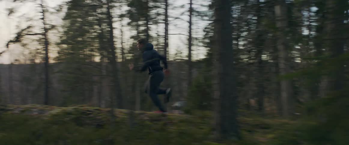 Man running fast on a trail through the woods in the mountains at sunset
