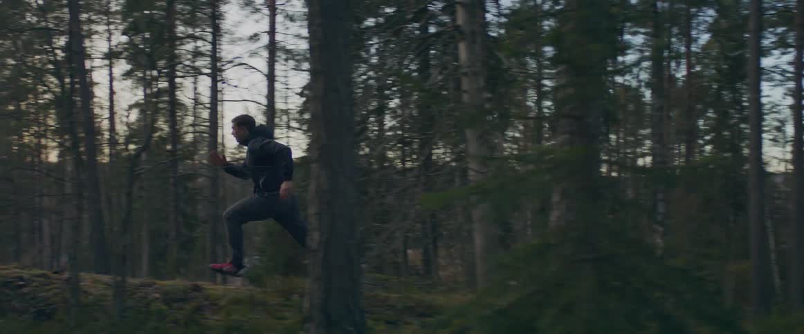 A man is jogging through the woods at dusk