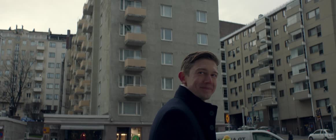 A young man smiles and turns around and walks towards an apartment building