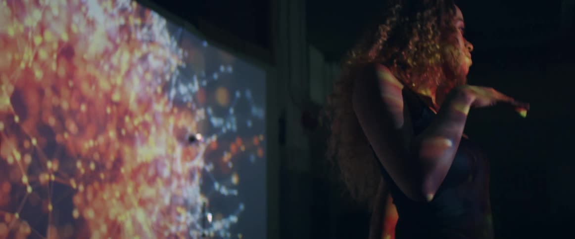 Young woman dancing slowly in front of a projector in a dimly lit room