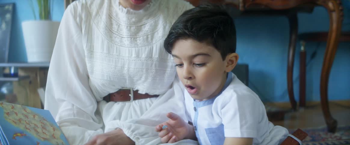 A mother reads a book to her son on the floor of a room as he gets excited with the story