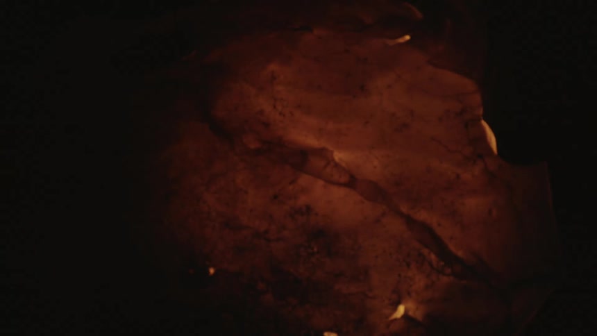 Flames glow yellow and orange enveloping material brightening surrounding darkness
