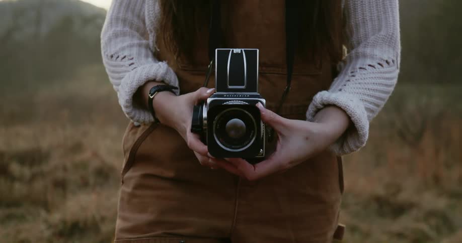 A woman holds a small older model of camera while making adjustments to it