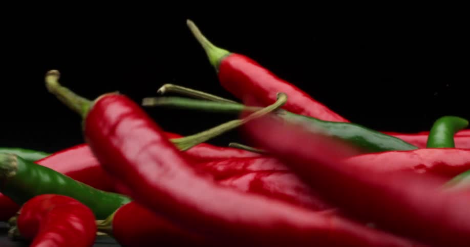 Red and green chili peppers falling on a gray surface with a black background