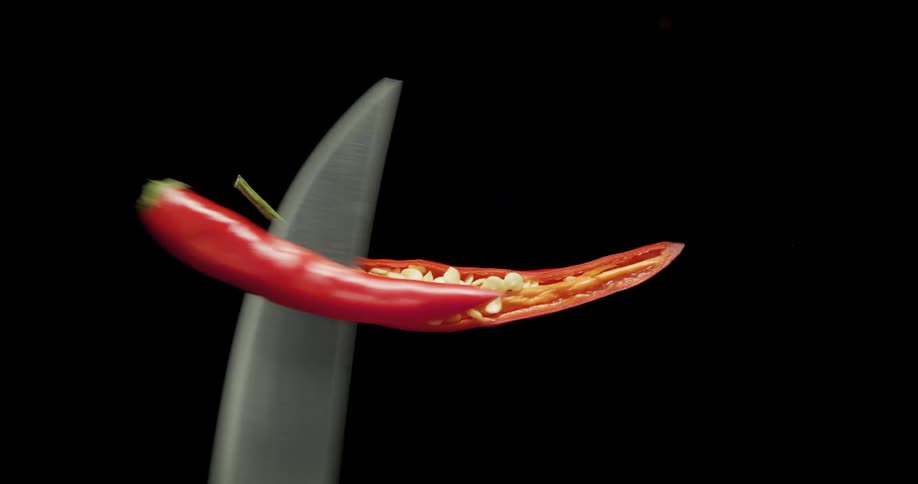 A sharp knife slicing a red chile pepper in half