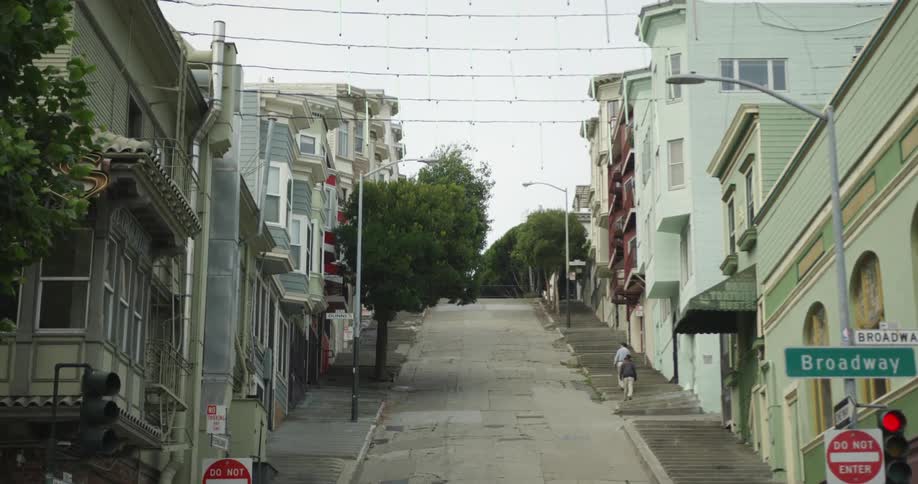 A wide shot of a city neighborhood on a hillside with pedestrians going uphill