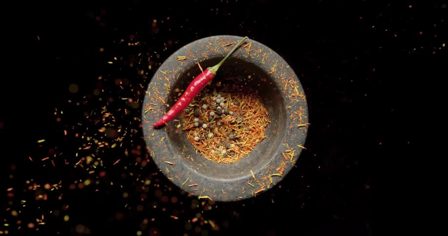 Spices fall in to a bowl with a chili pepper