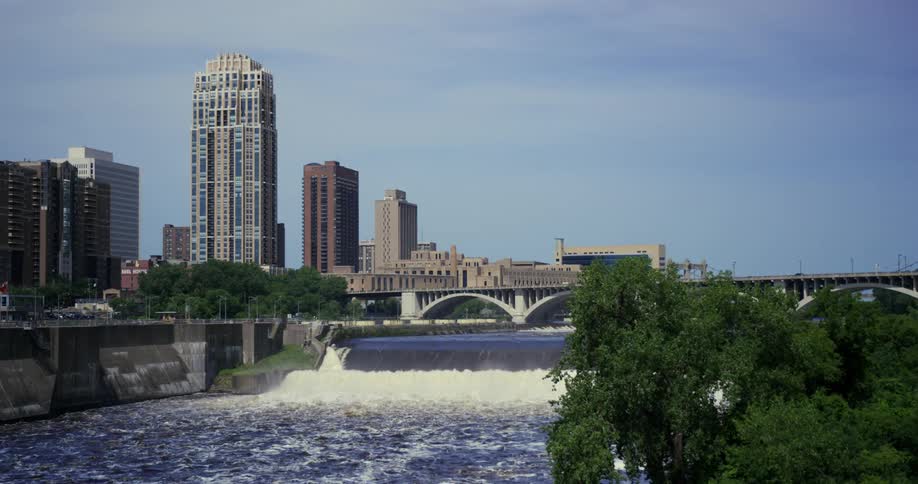 River flows down small falls near downtown city as traffic flows across bridge
