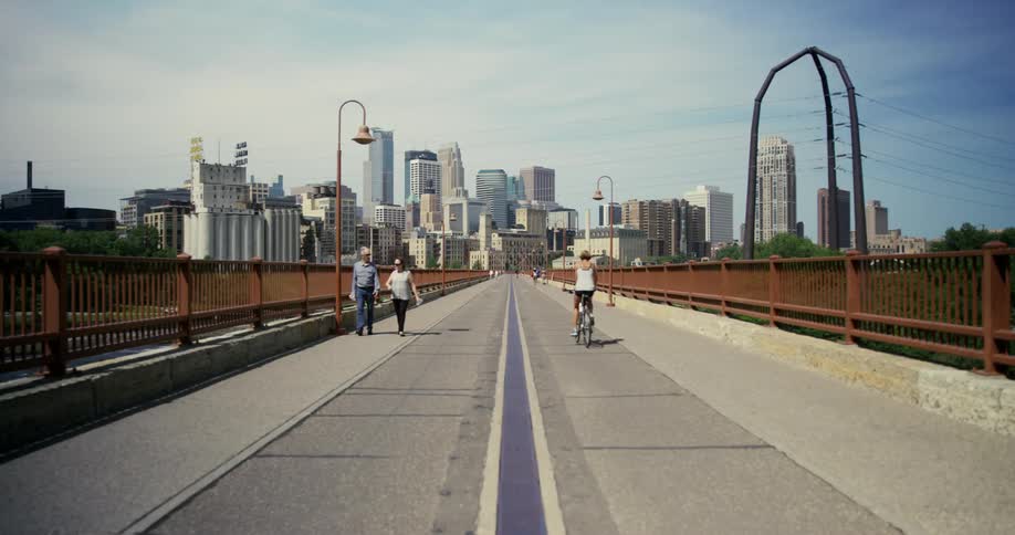 A bicyclist rides past an elderly couple holding hands as they walk on a pedestrian bridge near downtown