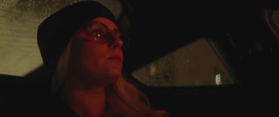 A young woman sits in a car at night as the rain falls