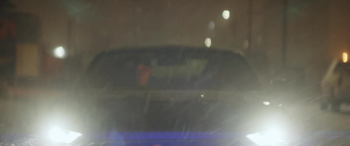 A pair of men travel through a city in a car on a snowy night