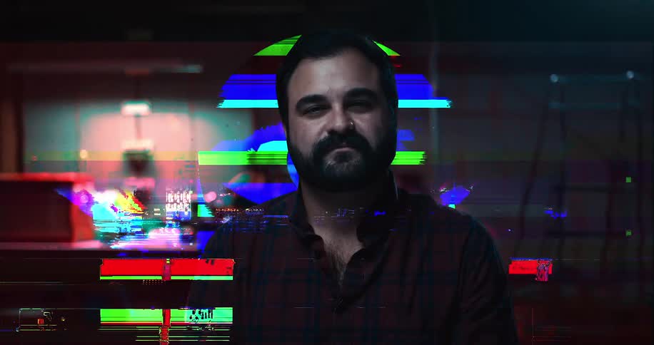 A man smiles in a dark room as a flashing computer screen is overlaid on him