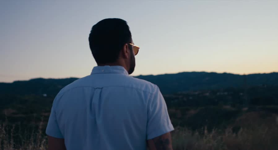 Man wearing sunglasses is standing outdoors viewing mountains at dusk