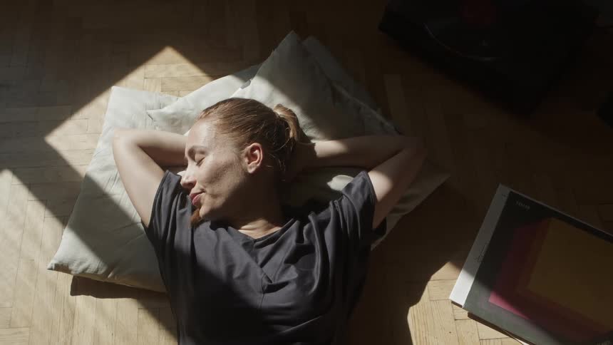 A woman naps on the floor with her arms behind her head
