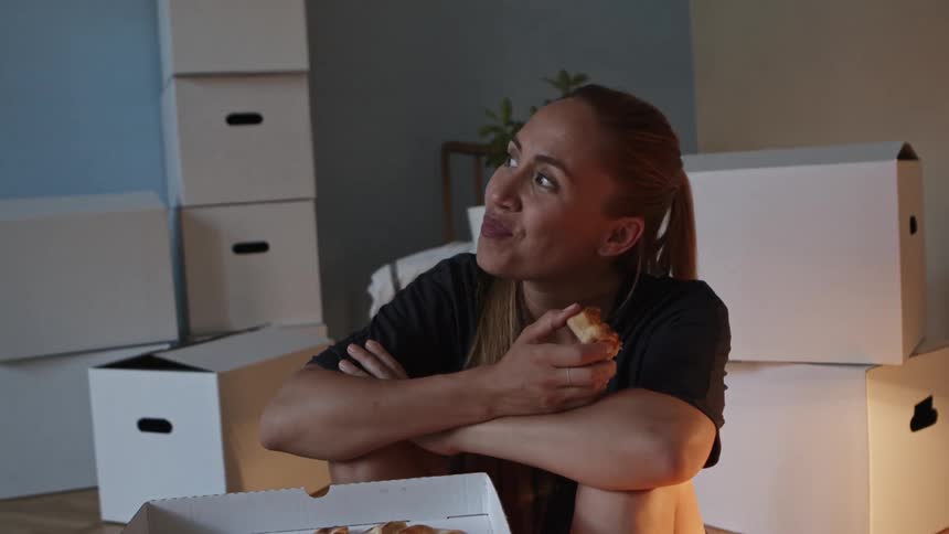 A woman is sitting on the floor while smiling and eating