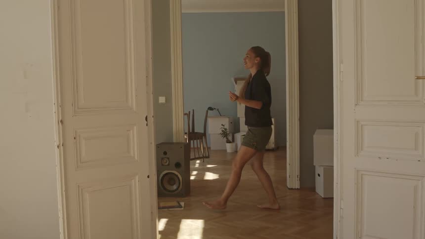 Woman with a ponytail a black blouse and shorts dances in a room at home