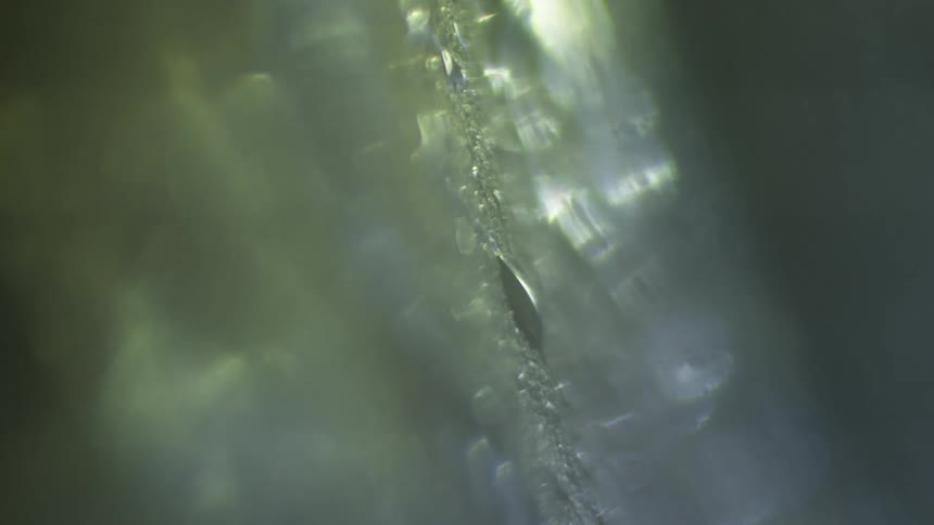 Vertical surface with liquid magnified and rain drops with light reflecting on area