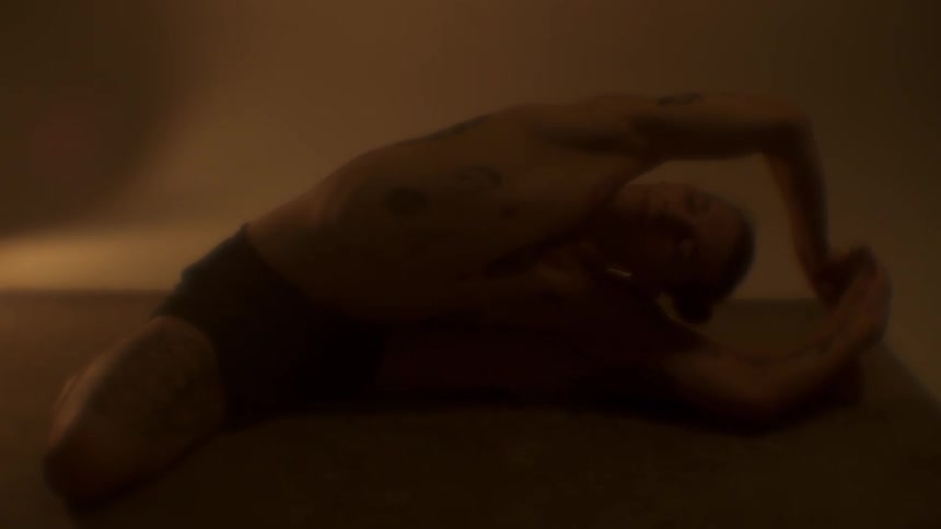 Tattooed strong fit man flexing in a yoga pose on a dimly lit room