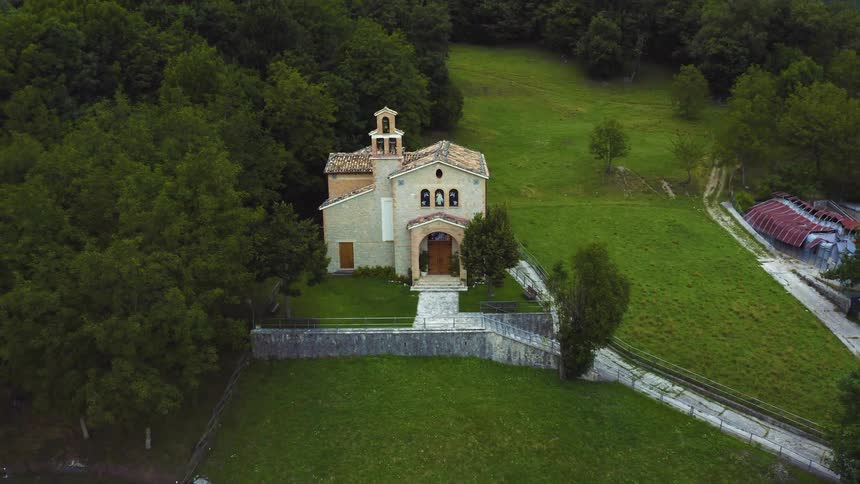 A church with a stone wall and paths on grassland and surrounded by trees and a couple other structures
