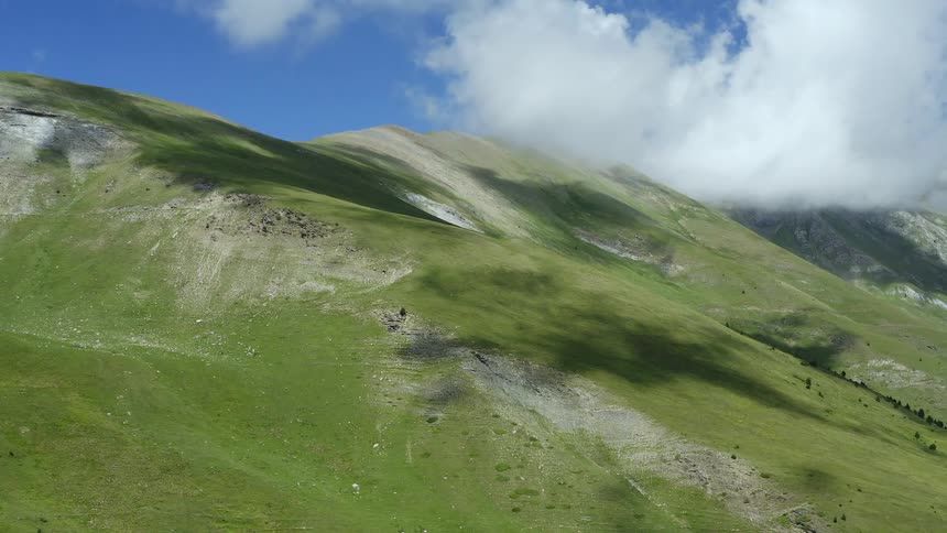 Wide shot of green mountains against a blue sky and some clouds during the day