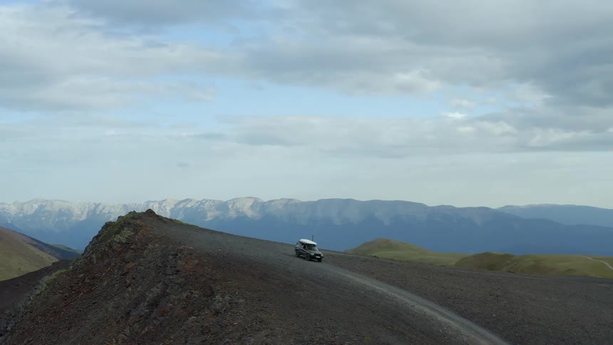 A vehicle parked atop a dirt ridge in the mountains on a cloudy day