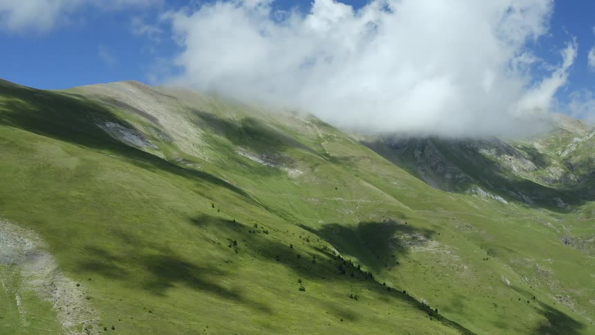 Large green hill mountains with white clouds moving across the top