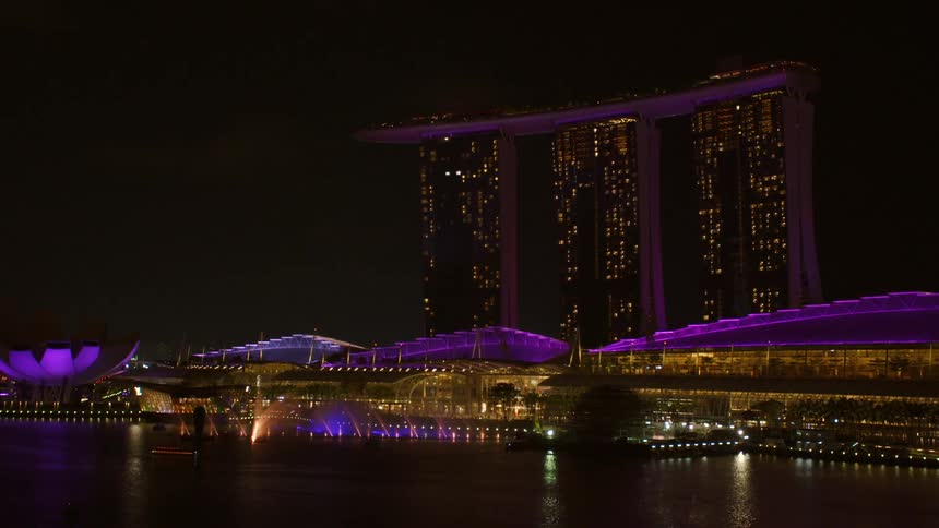 Landscape of a tall set of building displaying lights with smaller buildings below doing the same