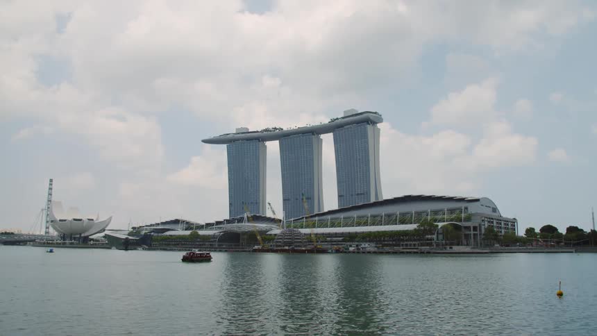 A boat in a body of water near the coast with buildings the sky and clouds in the background