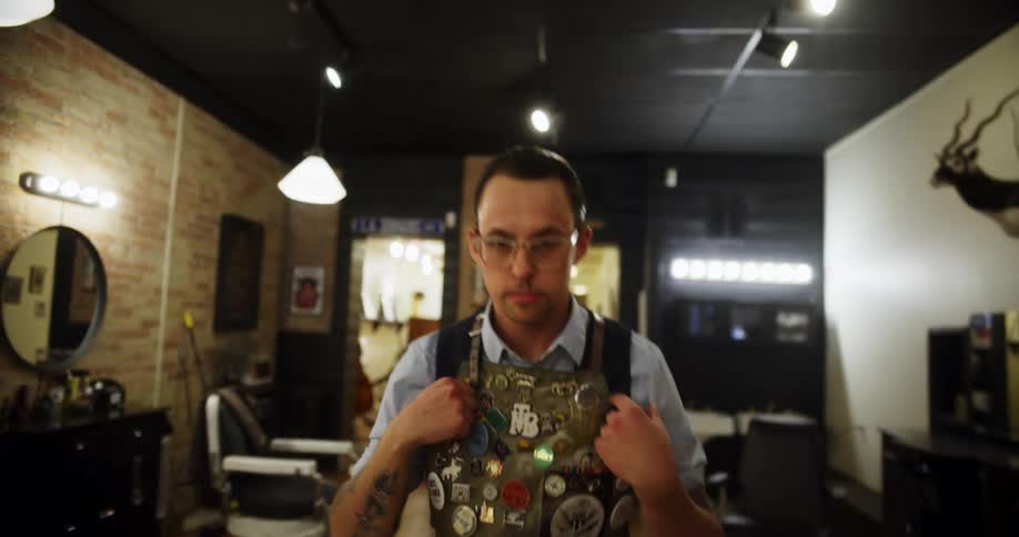 Man walks from back of barber shop past barber chairs to the front smiling