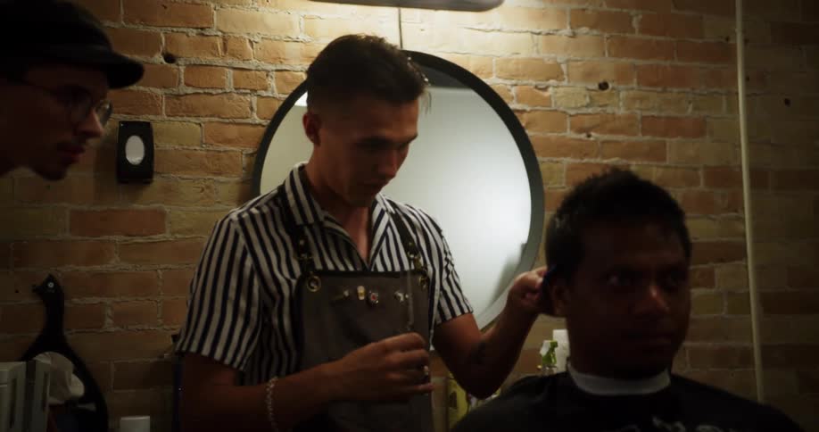 A barber trims a mans hair as other employees watch