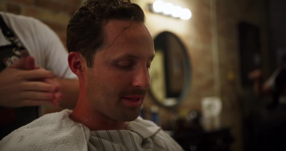 Barber rubs a towel over the recently shaved head of a customer in a barber shop