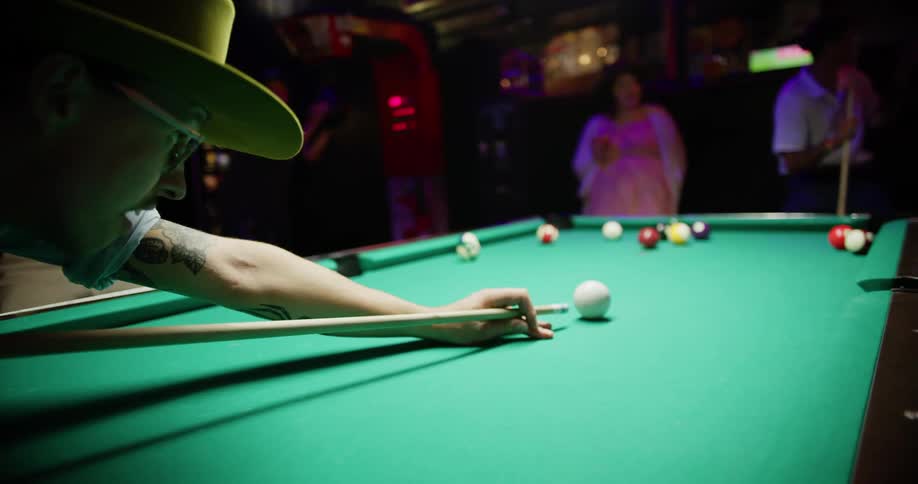 A man leans over a pool table and aims his shot with the pool stick