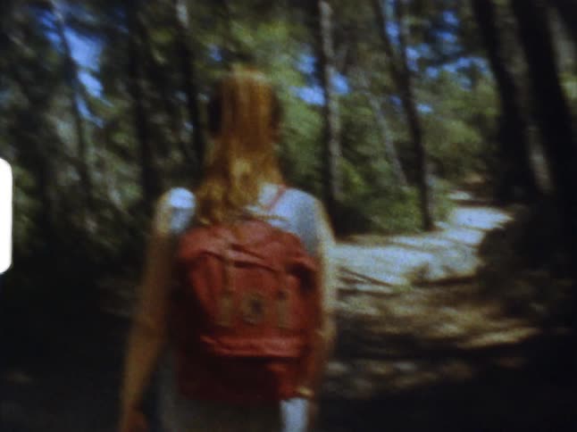 A female wearing a backpack hiking in the woods on 8mm