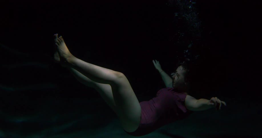 Young woman in a red swimsuit sinks to the bottom of a dark pool