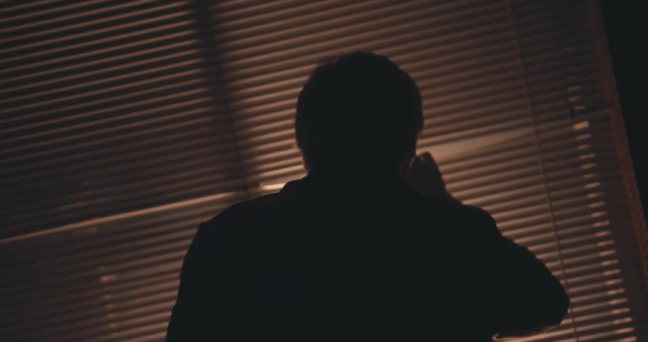 A man is looking out a window at night