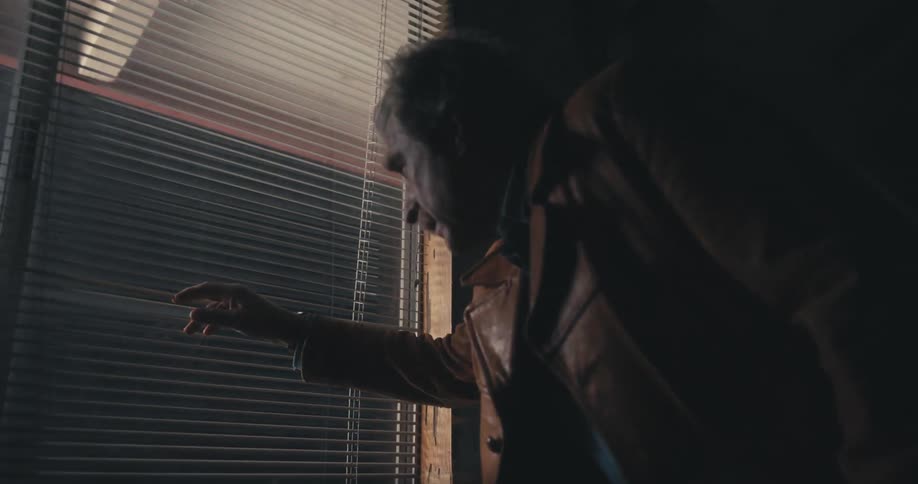 Old man looking through blinds at something
