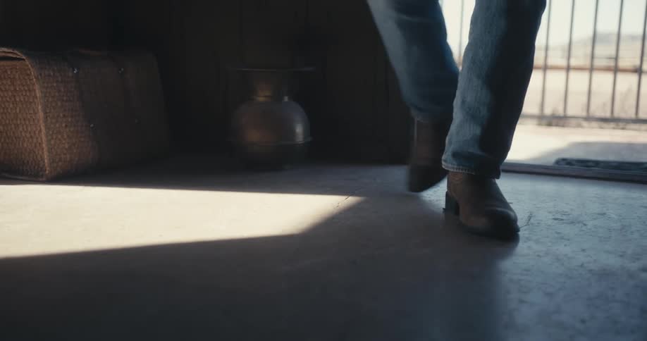 A person with jeans and boots opening a door and entering a room