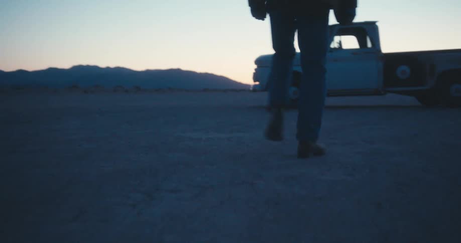 A man standing in the desert turns around and walks towards his truck and gets in