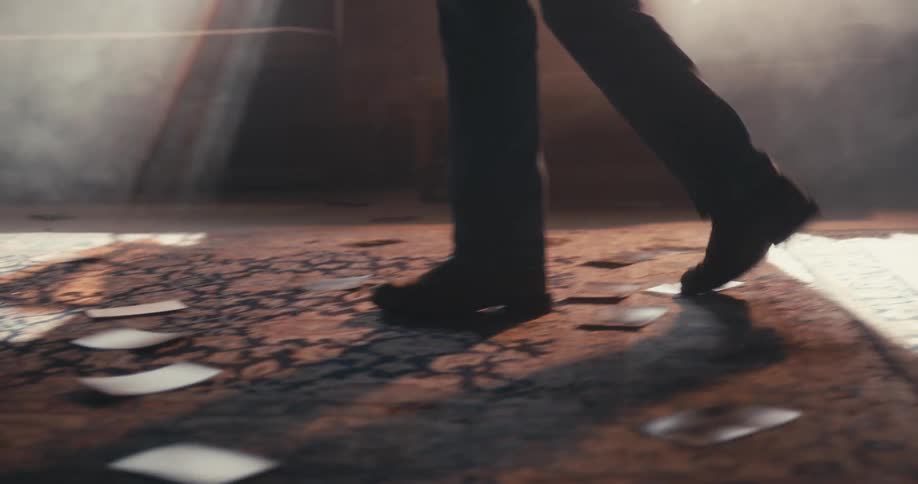 Person slowly walks and pauses to turn around with photographs on a floor rug in a dark room with sunlight coming in