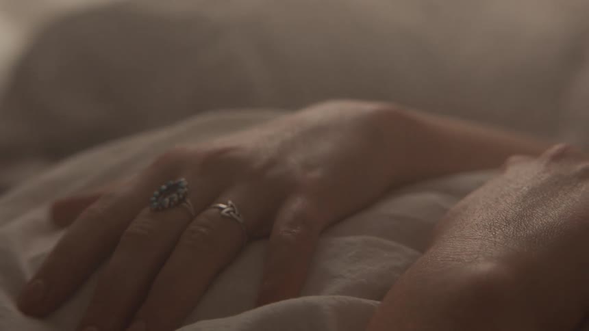 Close up of a womans hands on top of her sheets as she lies in bed