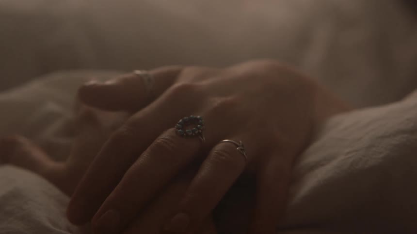 Two women with rings hold hands on top of blankets and sheets