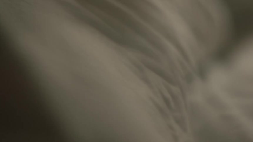 A person moving under a piece of wrinkled beige cotton cloth