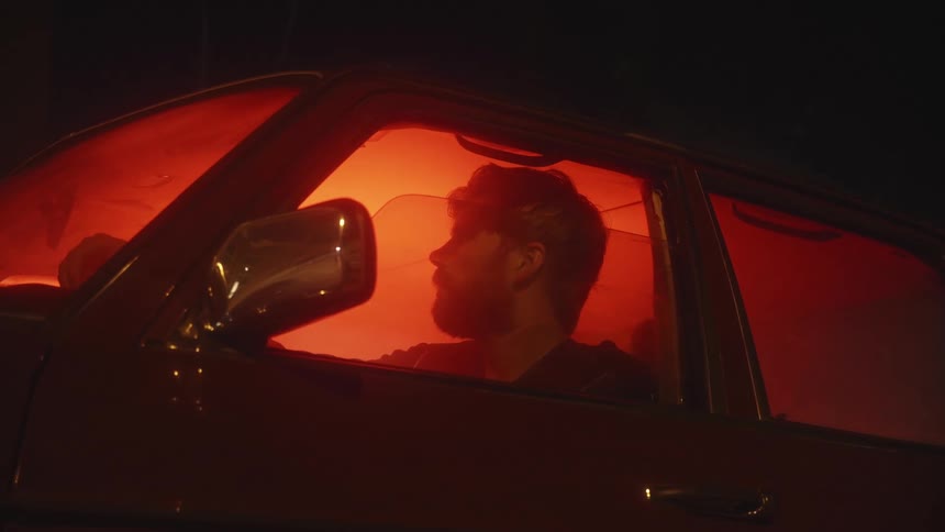 Man sitting in car with window down at night